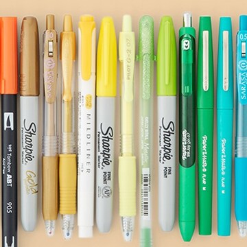 orange, yellow and green markers and pens in a row